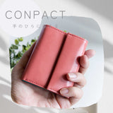 片手に収まるコンパクトなピンクの牛革財布を手に持つ