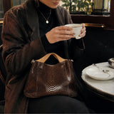 エトネのパイソンバッグを膝においおてお茶を飲む女性