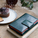 深い緑の二つ折り財布がカフェにある様子。バイカラーのピンクがちらりと見えてかわいい