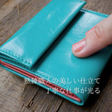 ターコイズブルーのコンパクト財布を指でなぞって、革の柔らかさを確かめている様子