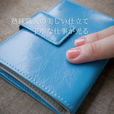 柔らかなイタリアンレザーで仕立てた、青い軽量二つ折り財布を指でなぞっているところ