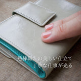 ライトグレーとターコイズブルーのバイカラーの二つ折り財布を指でなぞっている様子。柔らかさが伝わる。