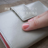 イタリアンレザーで仕立てた、グレーとピンクのバイカラーの軽量二つ折り財布を指でなぞっているところ