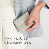 極小で薄い、ライトグレーのコンパクト財布をポケットにいれ入れようとしている様子