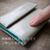 極小で薄い、ライトグレーのコンパクト財布を指の先でなぞるようにして良質な革を確かめている様子