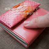 ピンクの仕立てがいい蛇革のお財布を指でなぞっている様子