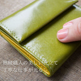 手のひらサイズお緑のコンパクト財布。お札を折らなくても使える人気の形を指でなぞっている。