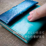 蛇革青いミニ財布を指でなぞって革の柔らかさを試している様子