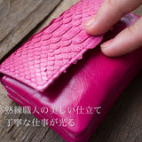 大人ピンクの、小さなカードサイズのコンパクト財布をそっと指で押して、柔らかい革が分かる様子