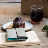 極小で薄い、ライトグレーのコンパクト財布がカフェの本の上にある様子