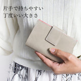 柔らかなイタリアンレザーで仕立てた、グレーとピンクの軽量二つ折り財布を手で持っているところ