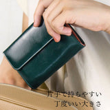 深い緑とピンクのバイカラーの二つ折り財布をバッグに入れる様子