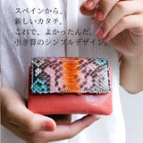 職人の腕が光る、仕立ての良いパイソン蛇革のピンクのミニ財布を手で包み込むように持っている