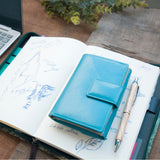 青の牛革財布がノートの上に添えられている様子|超軽量で大容量な二つ折り財布