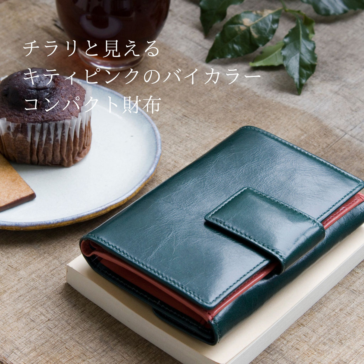深い緑の二つ折り財布がカフェにある様子。バイカラーのピンクがちらりと見えてかわいい
