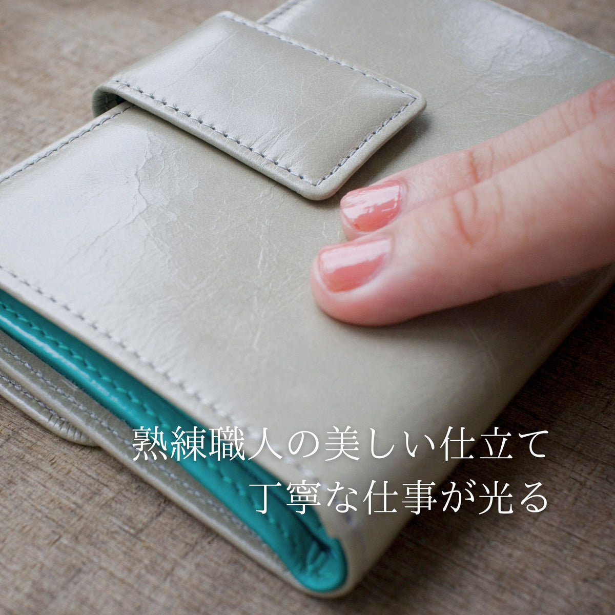 ライトグレーとターコイズブルーのバイカラーの二つ折り財布を指でなぞっている様子。柔らかさが伝わる。