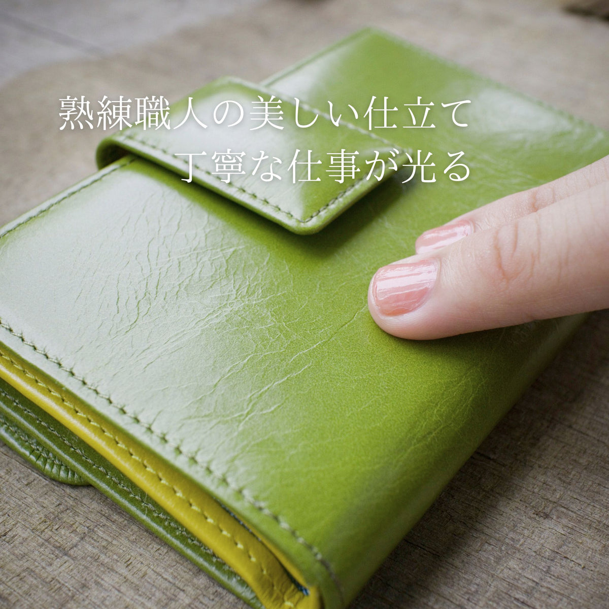 黄緑色の二つ折り財布の革の柔らかさを指で確かめている様子