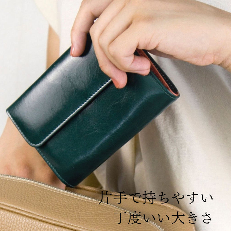 深い緑とピンクのバイカラーの二つ折り財布をバッグに入れる様子